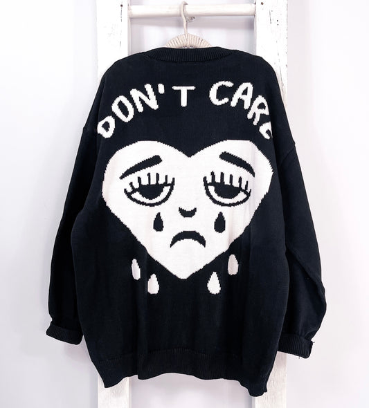 Black knitted cardigan with "don't care" printed on and crying heart face design