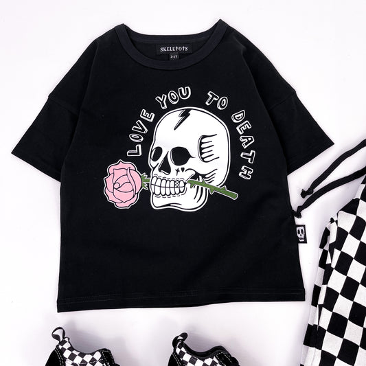 Kids black t shirt with "love you to death" printed on and a design of a skull holding a rose in its teeth