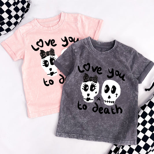 Kids distressed style pink tee shirt with "Love you to death" printed on and 2 skulls, one with a black ribbon