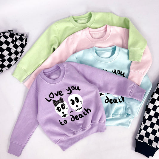 Kids pastel pink sweatshirt with "Love you to death" printed on and 2 skulls, one with a black ribbon