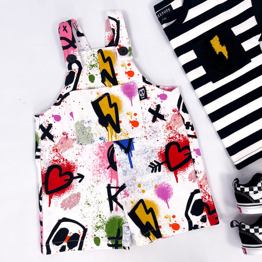 Kids white short dungarees with colourful graffiti print skulls, hearts, lightning bolts and paint splatter