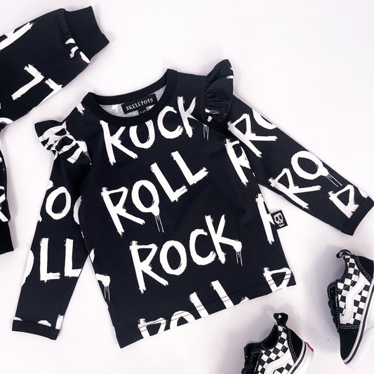 Kids black long sleeved sweatshirt with frilled shoulder detail and words "rock" and "roll" printed on it repeatedly